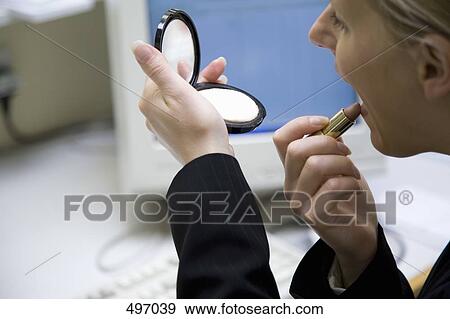 Stock Photo - Detail of a woman holding a mirror compact and applying lipstick. Fotosearch