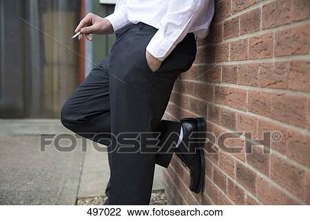 Low section of a businessmen leaning against a wall and smoking a cigarette View Large Photo Image Stock Image - Low section of a businessmen leaning against a wall and smoking a cigarette. Fotosearch