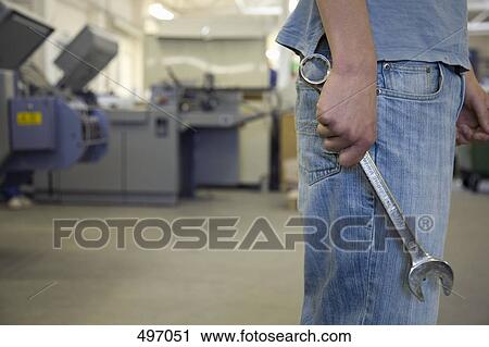 Midsection of a man standing in a factory with a wrench View Large Photo Image Stock Image - Midsection of a man standing in a factory with a wrench. Fotosearch