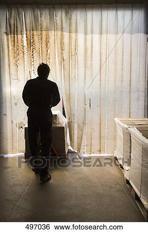Stock Photograph - Silhouette of a man pushing a forklift through a plastic doorway. Fotosearch