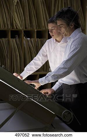 Two businessmen standing over a light box in an office View Large Photo Image Stock Image - Two businessmen standing over a light box in an office. Fotosearch