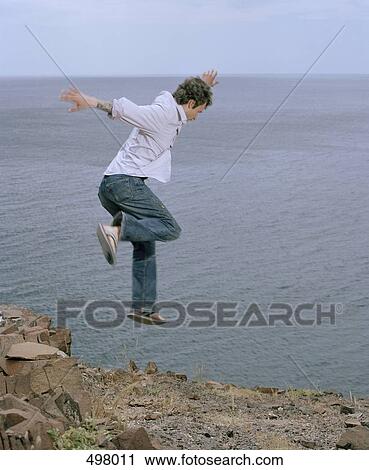 Stock Image - A man jumping off a cliff near the sea. Fotosearch