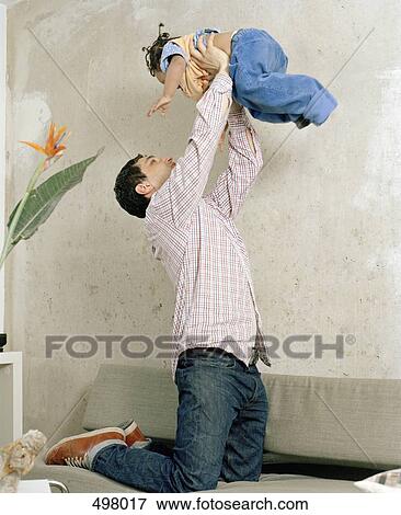 A man kneeling on a sofa and holding a toddler in the air View Large Photo Image Stock Photo - A man kneeling on a sofa and holding a toddler in the air. Fotosearch