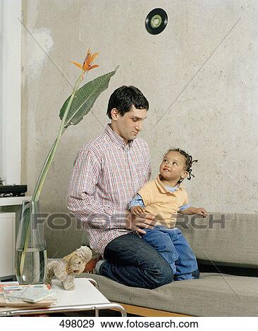 A man kneeling with a toddler on a sofa View Large Photo Image Stock Photo - A man kneeling with a toddler on a sofa. Fotosearch