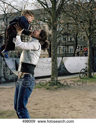 Stock Photo - A woman picking up a toddler in a park. Fotosearch