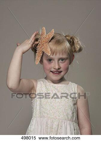 Stock Photography - A young girl holding a starfish against her head. Fotosearch