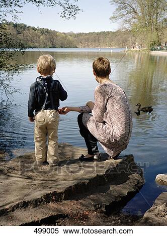 Stock Photography - A mother and son feeding ducks by a lake. Fotosearch