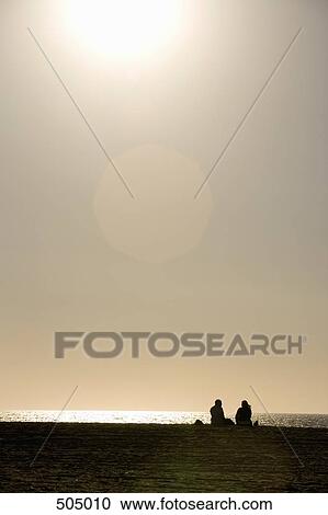 A couple sitting on the beach at sunset View Large Photo Image Stock Image - A couple sitting on the beach at sunset. Fotosearch