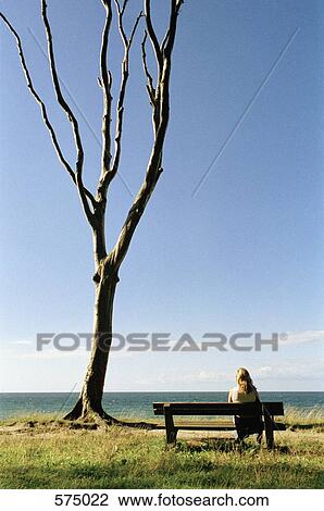 Stock Image - A woman sitting on a bench and looking out to sea. Fotosearch