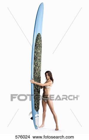 Picture - A woman standing holding a surfboard. Fotosearch