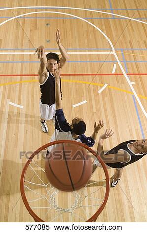 Stock Photography - A basketball player shooting a basket and two more players playing defense. Fotosearch