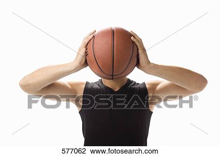 Stock Image - A studio portrait of a young man holding a basketball in front of his face. Fotosearch