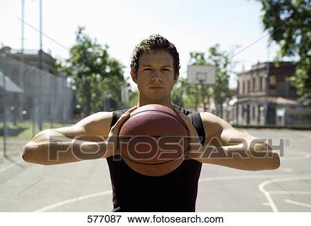 Stock Photo - A young man at an outdoor basketball court preparing to throw the ball. Fotosearch
