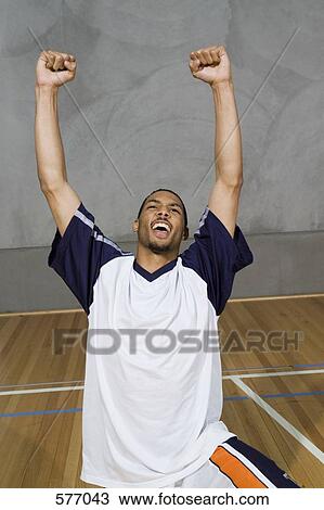 Stock Image - A young man kneeling with his arms raised in victory. Fotosearch