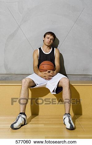 Stock Image - A young man sitting on a bench on a basketball court. Fotosearch