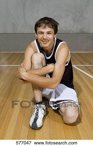 Stock Photo - A young man sitting with his arm around one knee. Fotosearch