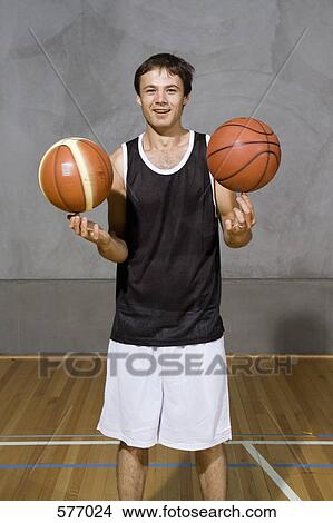 Picture - A young man spinning two basketballs on his fingers. Fotosearch