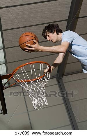 Stock Photo - A young man standing above basketball hoop holding ball. Fotosearch
