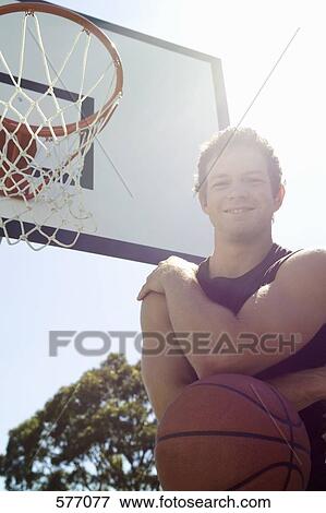 Stock Photo - A young man standing near an outdoor basketball hoop. Fotosearch