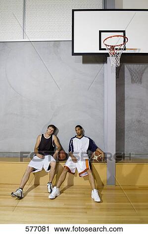 Stock Image - Two young men sitting on a bench at a basketball court. Fotosearch