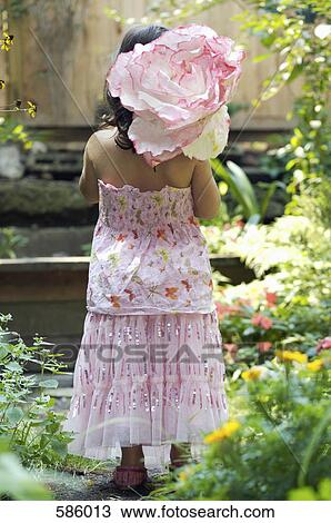 Stock Image - A Rear View of a young girl dressed up standing in a garden and carrying a paper flower. Fotosearch