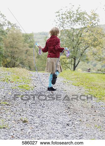 A rear view of a young girl jumping road on a gravel path in the country View Large Photo Image Stock Photo - A rear view of a young girl jumping road on a gravel path in the country. Fotosearch
