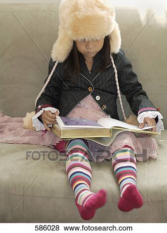 A young girl in funny clothes sitting on a couch reading a book View Large Photo Image Stock Photo - A young girl in funny clothes sitting on a couch reading a book. Fotosearch
