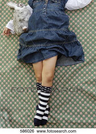 Stock Photograph - A young girl with an obscured face lying on a patterned sheet with a stuffed toy. Fotosearch