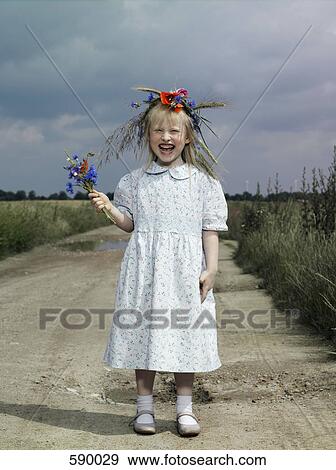Stock Photo - A girl standing on a country road and holding wildflowers. Fotosearch