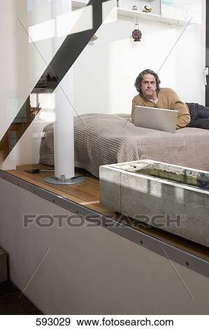 A man lying on his bed using a laptop View Large Photo Image Stock Photo - A man lying on his bed using a laptop. Fotosearch