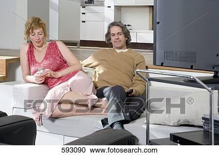 A woman using a mobile phone next to a man watching television View Large Photo Image Stock Image - A woman using a mobile phone next to a man watching television. Fotosearch