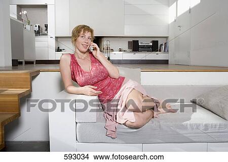 Picture - A woman using her mobile phone and sitting on the sofa. Fotosearch