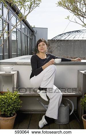 Picture - A young woman drinking coffee on a rooftop garden. Fotosearch