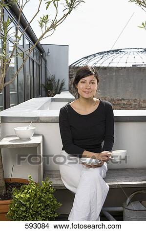 Picture - A young woman drinking coffee on a rooftop garden. Fotosearch
