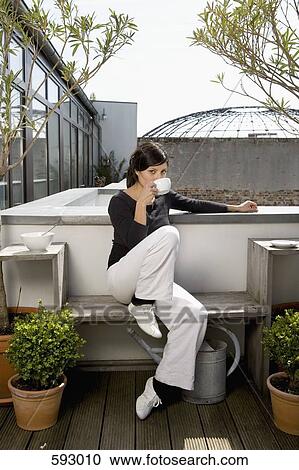 Stock Image - A young woman drinking coffee on a rooftop garden. Fotosearch