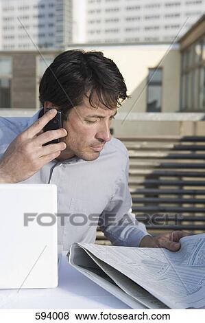 A businessman sitting on a rooftop terrace with a newspaper, mobile phone and laptop View Large Photo Image Stock Photo - A businessman sitting on a rooftop terrace with a newspaper, mobile phone and laptop. Fotosearch