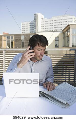 A businessman sitting on a rooftop terrace with a newspaper, mobile phone and laptop View Large Photo Image Stock Photo - A businessman sitting on a rooftop terrace with a newspaper, mobile phone and laptop. Fotosearch