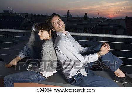 A couple sitting back to back on a rooftop terrace at night View Large Photo Image Picture - A couple sitting back to back on a rooftop terrace at night. Fotosearch