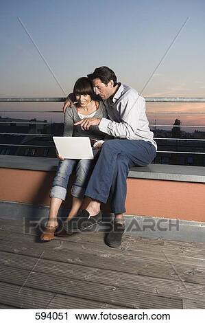 A couple using a laptop computer on a rooftop terrace View Large Photo Image Stock Image - A couple using a laptop computer on a rooftop terrace. Fotosearch