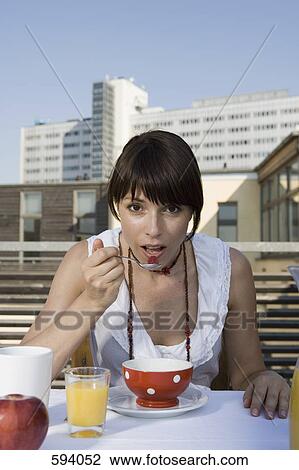 Stock Image - A woman eating breakfast on a rooftop terrace. Fotosearch