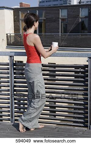 A woman standing on a rooftop terrace with a cup View Large Photo Image Stock Photo - A woman standing on a rooftop terrace with a cup. Fotosearch