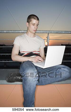 A young adult man using a laptop computer on a rooftop terrace View Large Photo Image Picture - A young adult man using a laptop computer on a rooftop terrace. Fotosearch