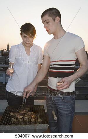 Stock Photo - A young couple having a barbeque on a rooftop terrace. Fotosearch