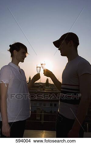 A young couple toasting with champagne on a rooftop terrace at sunset View Large Photo Image Picture - A young couple toasting with champagne on a rooftop terrace at sunset. Fotosearch