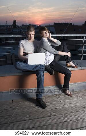 Stock Photo - A young couple using a laptop computer on a rooftop terrace. Fotosearch