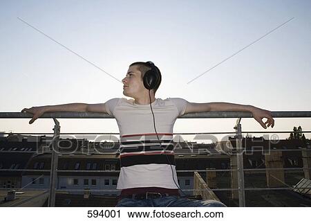 A young man sitting on a rooftop wearing headphones View Large Photo Image Stock Image - A young man sitting on a rooftop wearing headphones. Fotosearch