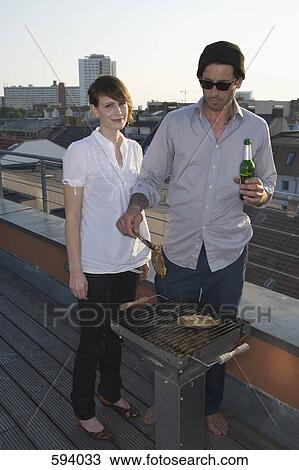 Stock Image - Two People having a barbeque on a rooftop terrace. Fotosearch