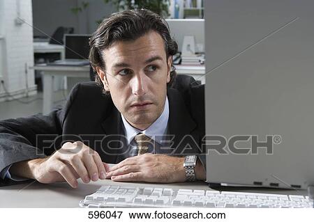Stock Photo - A businessman hiding behind a computer. Fotosearch
