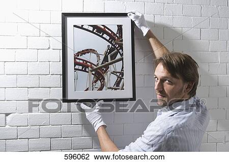 A man hanging a framed photograph on a wall View Large Photo Image Stock Image - A man hanging a framed photograph on a wall. Fotosearch