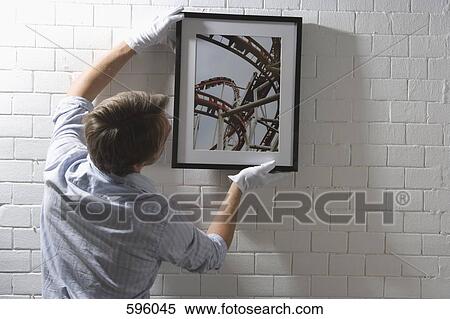 A man hanging a framed photograph on a wall View Large Photo Image Stock Photography - A man hanging a framed photograph on a wall. Fotosearch